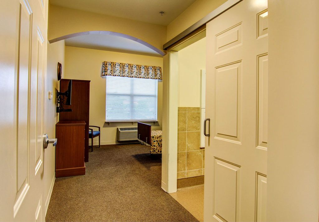 A cozy bedroom with a carpeted floor, featuring a bed, window, and furniture.