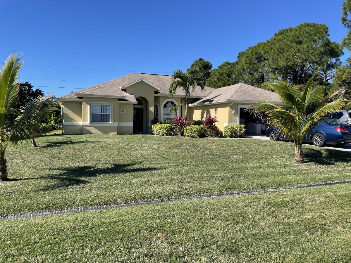 A single-story house with a well-maintained lawn and palm trees under a clear blue sky.