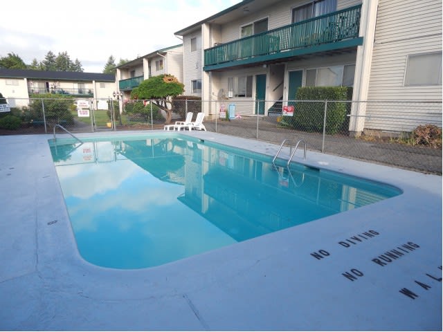 An outdoor swimming pool at an apartment complex with surrounding fence and deck chairs.