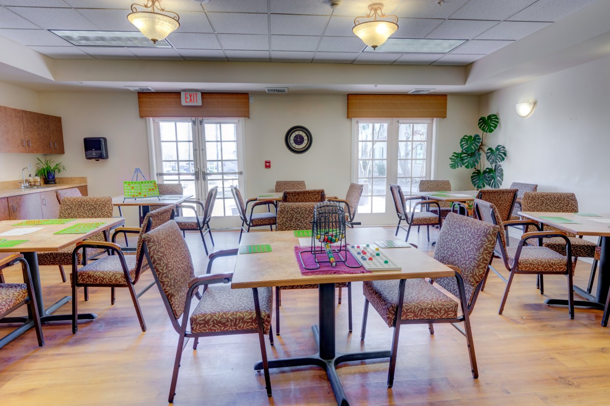 A cozy dining area with neatly arranged tables and chairs, surrounded by large windows and decorative plants.