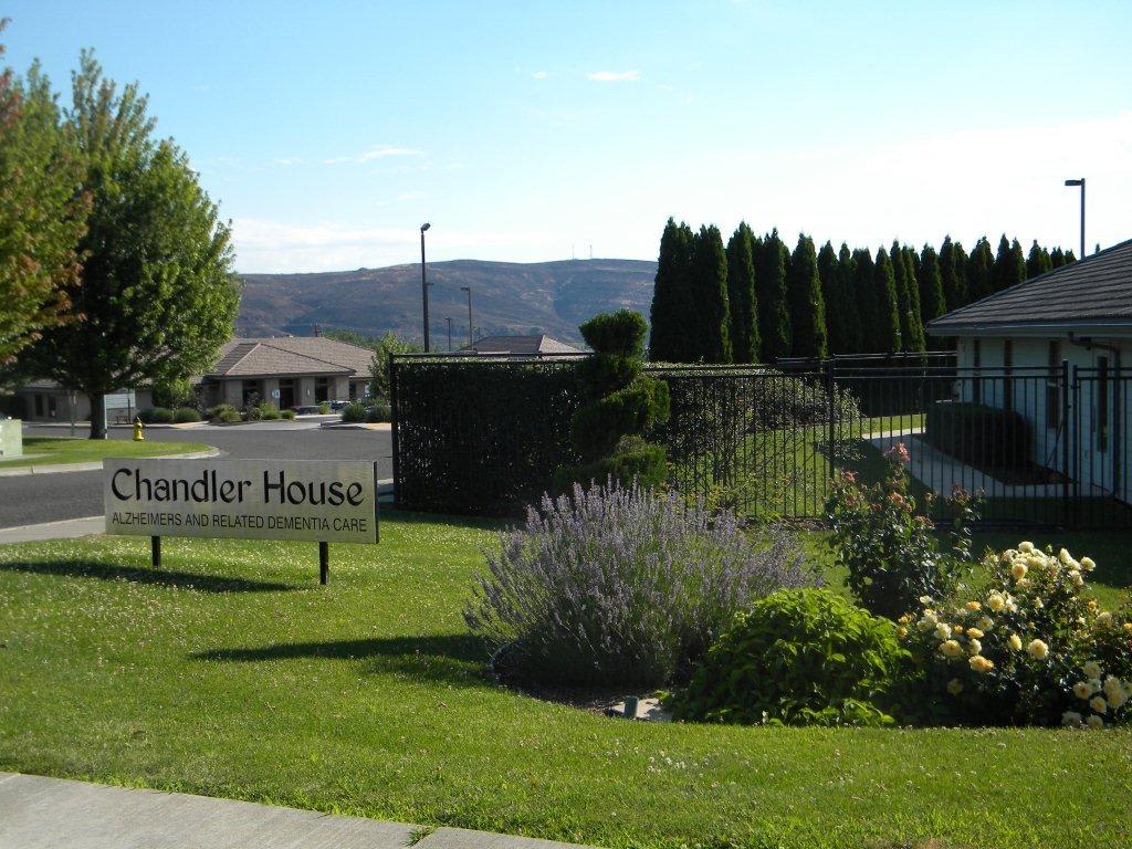 Scenic view of a building with a sign reading 'Chandler House' surrounded by lush greenery and hills in the background.