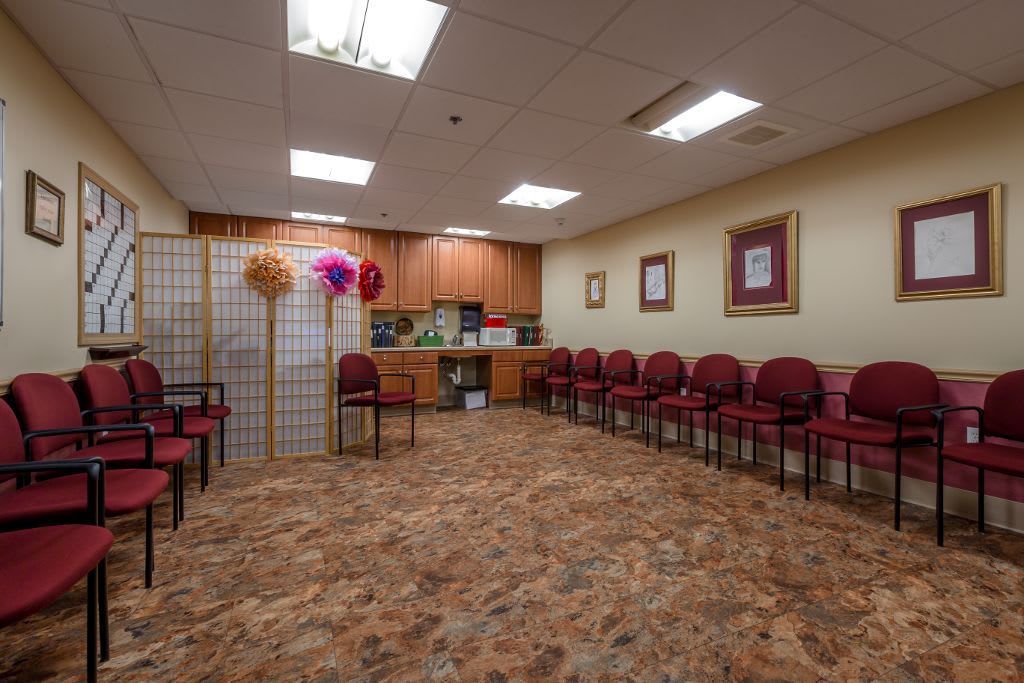 A spacious waiting room with multiple chairs arranged along the walls, featuring warm lighting and decorative elements.