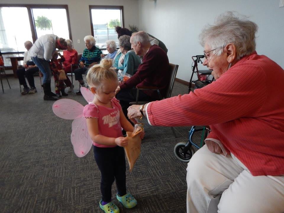 A child in a fairy costume interacting with an elderly person indoors.