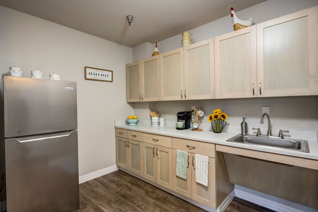 A modern kitchen with light wooden cabinets, a sleek refrigerator, and a countertop featuring a coffee maker and sunflowers.