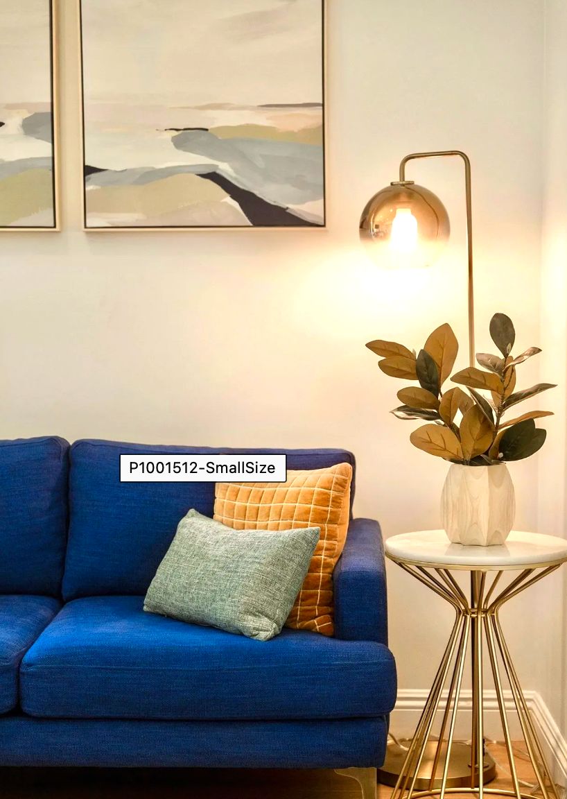 A cozy living room setup featuring a blue sofa with decorative cushions, a sleek floor lamp, indoor plant on a side table, and wall art.