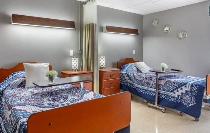 A well-organized hospital room with two beds, each featuring a bedside table and lamp.