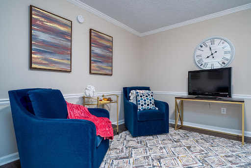 A cozy living room featuring blue chairs, modern wall art, and a television set against a neutral backdrop.