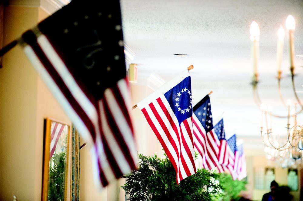 A row of American flags, including the historic Betsy Ross flag, displayed indoors.