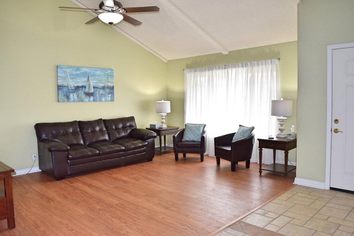 A cozy living room with a brown leather sofa, two chairs, lamps on either side, and a ceiling fan above.