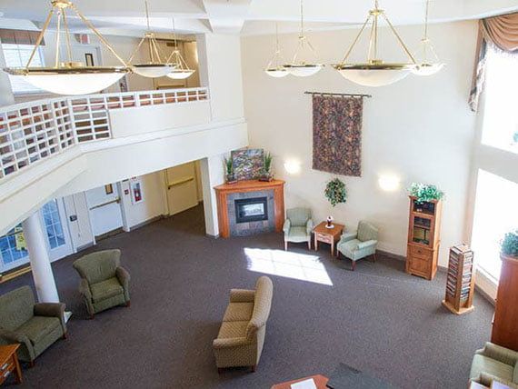 A spacious, modern lobby with a two-story ceiling, featuring a seating area with comfortable chairs and sofas, a fireplace, chandeliers, and decorative elements.