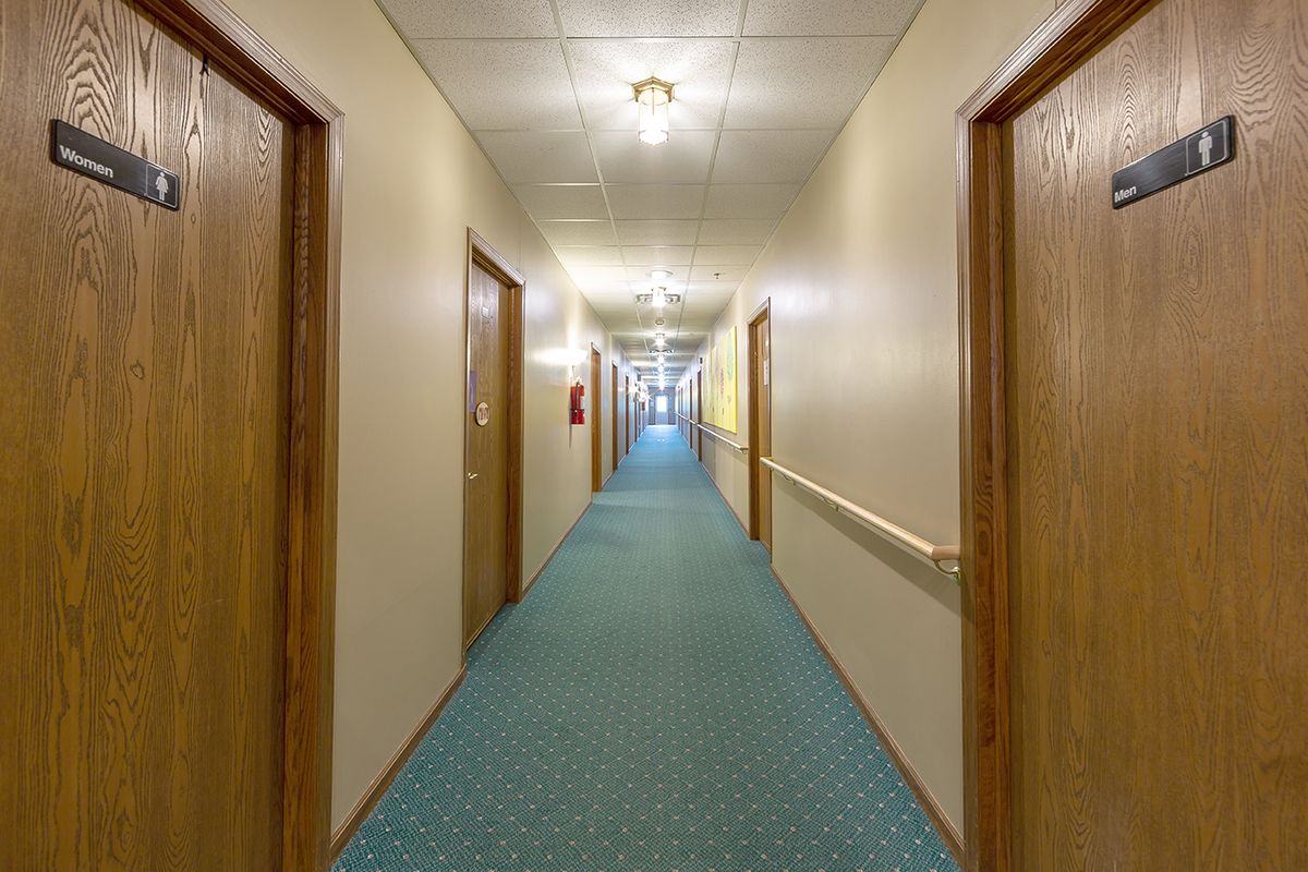 A long, empty hallway with closed wooden doors and a blue carpet.