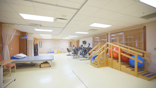 A spacious gym area equipped with various exercise machines, wooden stairs, and a stability ball for fitness and rehabilitation.