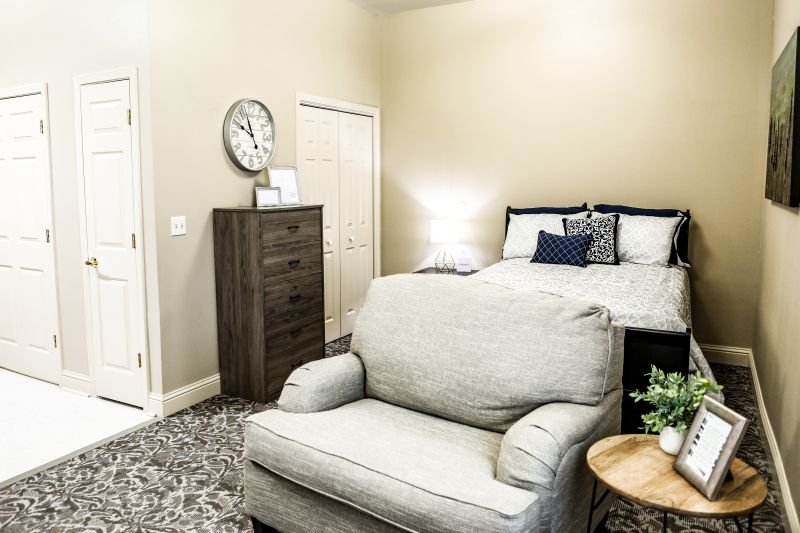 A cozy bedroom with a bed, armchair, dresser, and a clock on the wall.