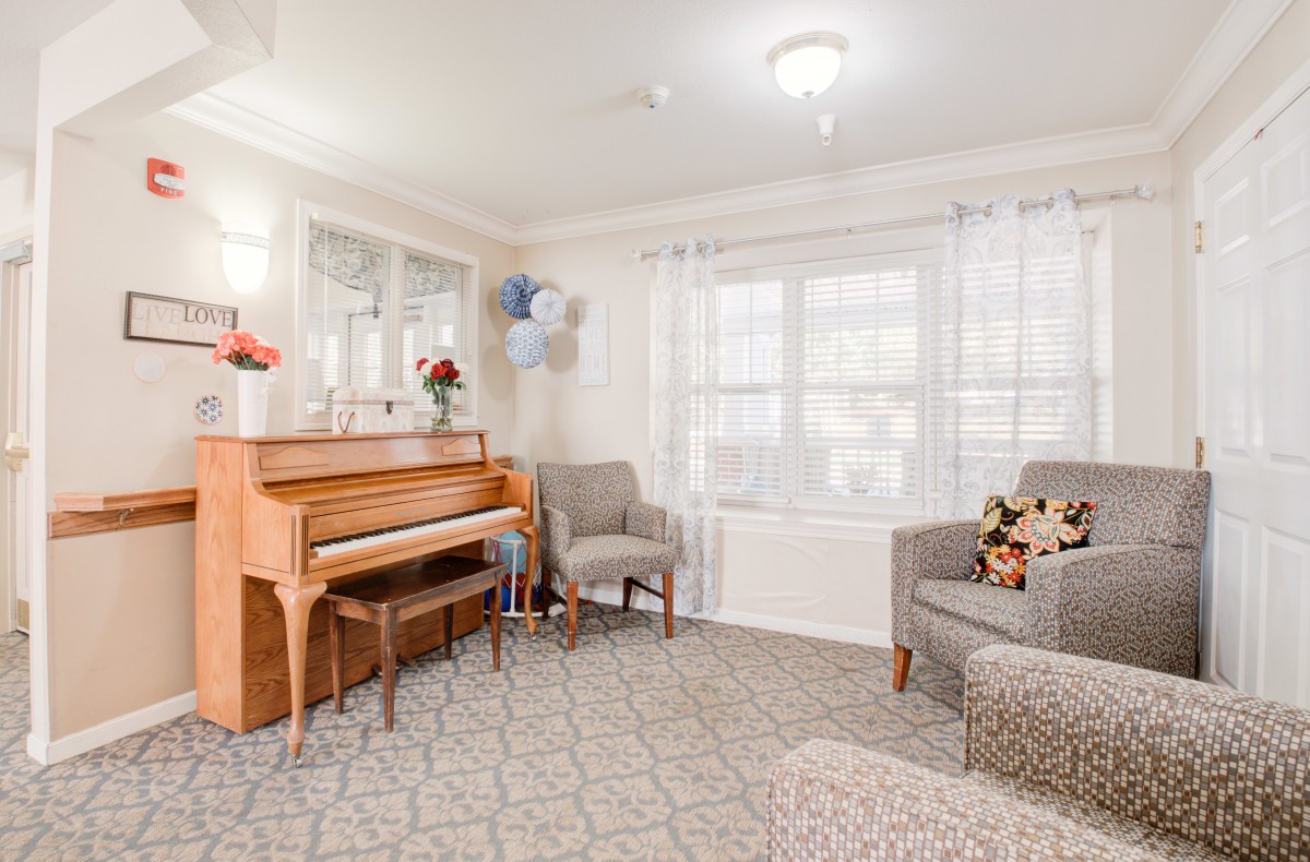 A cozy living room with a piano, comfortable chairs, and bright natural light.