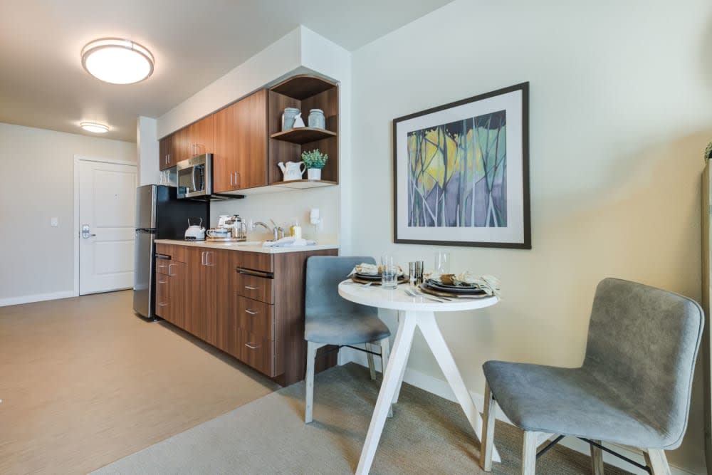 A modern kitchen with wood cabinets, featuring a cozy dining area with a round table and chairs, complemented by artwork on the wall.