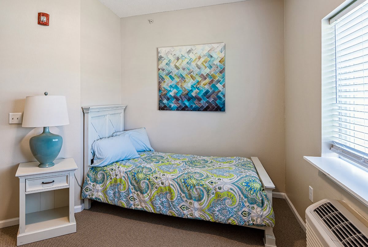 A cozy bedroom with a colorful quilt and abstract artwork above the bed.