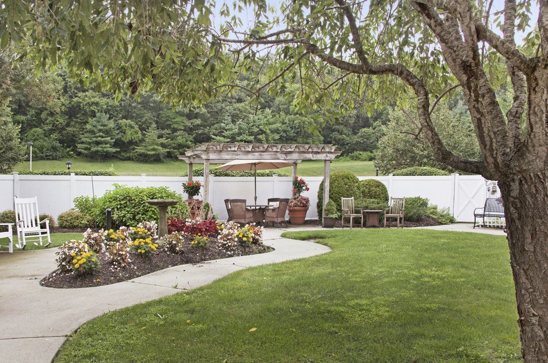 A serene backyard garden with a patio, chairs, and a pathway surrounded by lush greenery and colorful flowers.