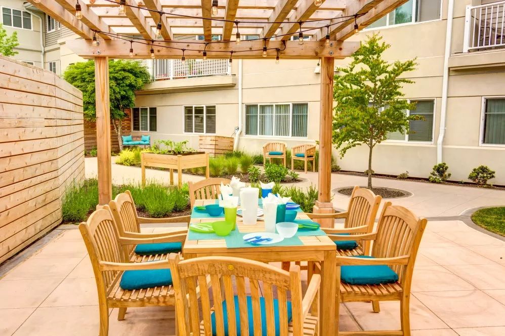 An inviting outdoor patio features a wooden dining set under a pergola, surrounded by lush garden landscaping.