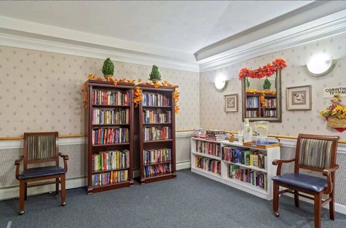 A cozy library nook with bookshelves filled with books, decorated with floral accents and featuring comfortable seating.