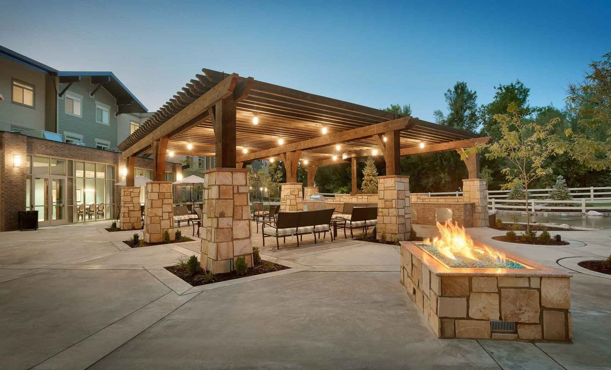 A cozy outdoor patio with a pergola and fire pit illuminated by string lights.