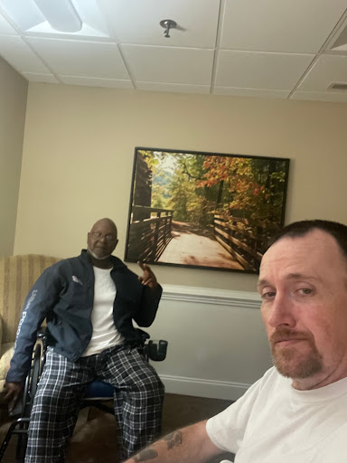 A friendly selfie shared between two individuals, one in a wheelchair, enjoying time together indoors.