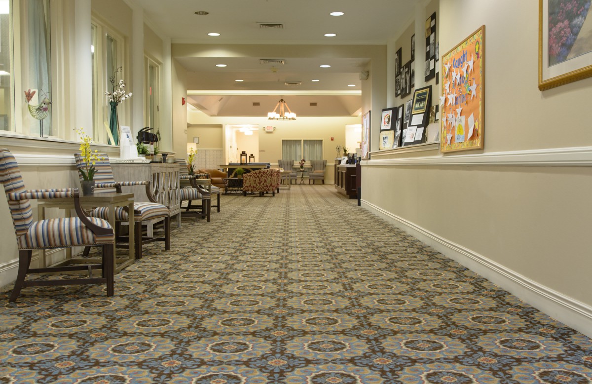 A well-lit hallway with patterned carpeting and chairs lined along the walls.