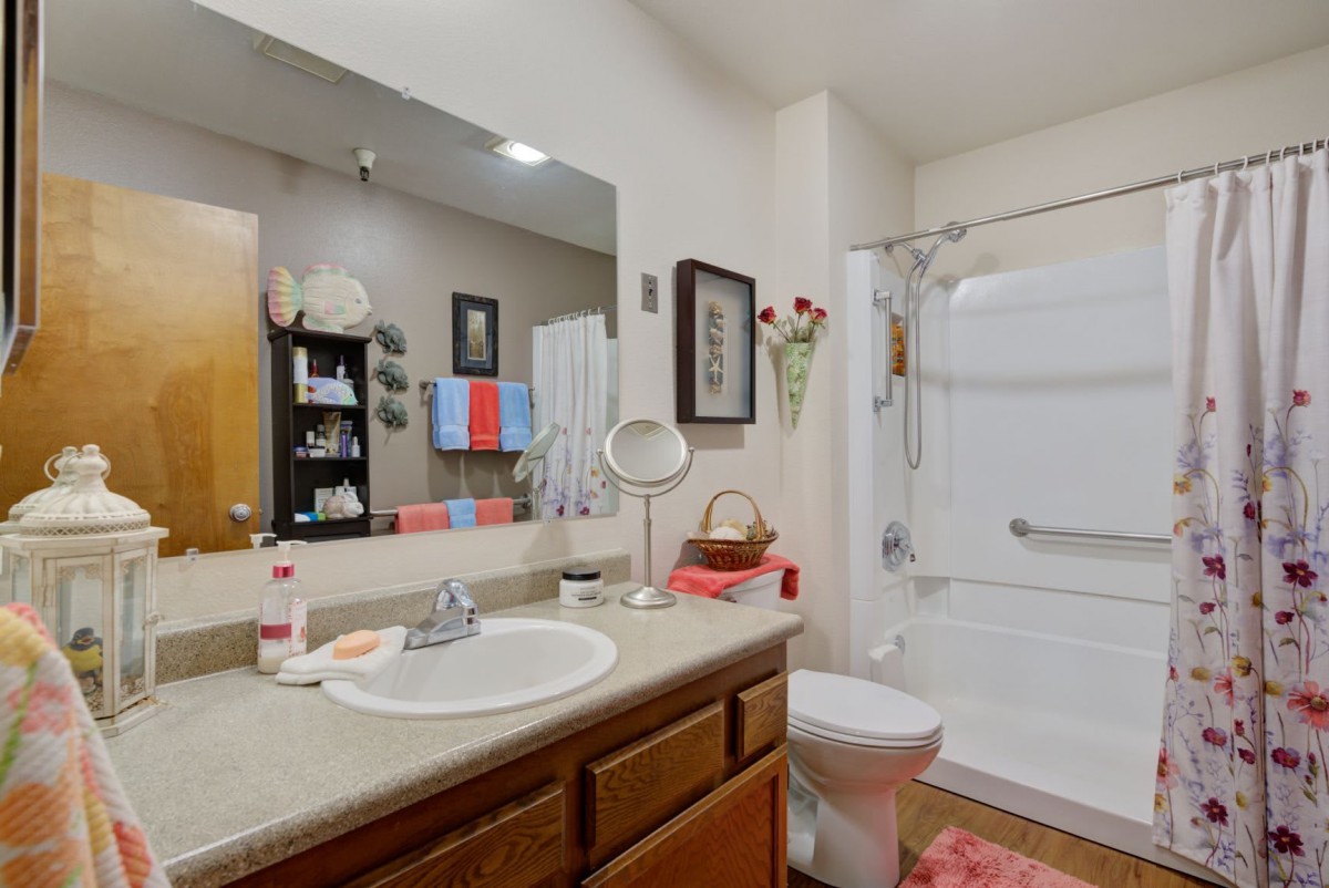 A clean and organized bathroom featuring a large mirror, sink, toilet, shower, and neatly arranged towels.