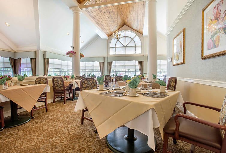 A well-lit restaurant dining room with elegantly set tables and large windows.