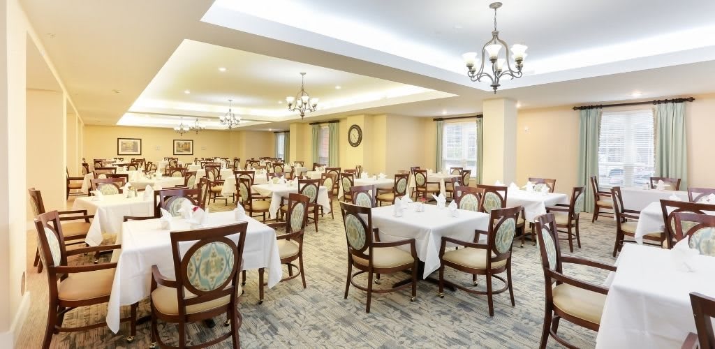 A well-lit dining area with elegantly arranged tables and chairs, featuring chandeliers and classic decor.