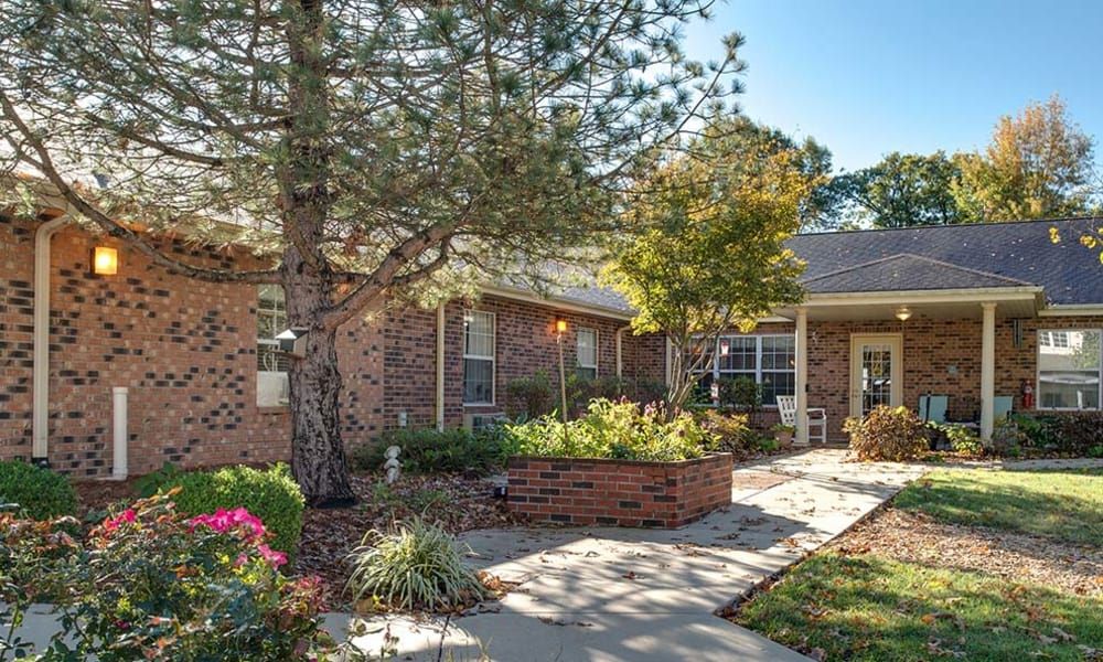 A well-maintained brick house with a landscaped front garden and a walkway surrounded by trees.