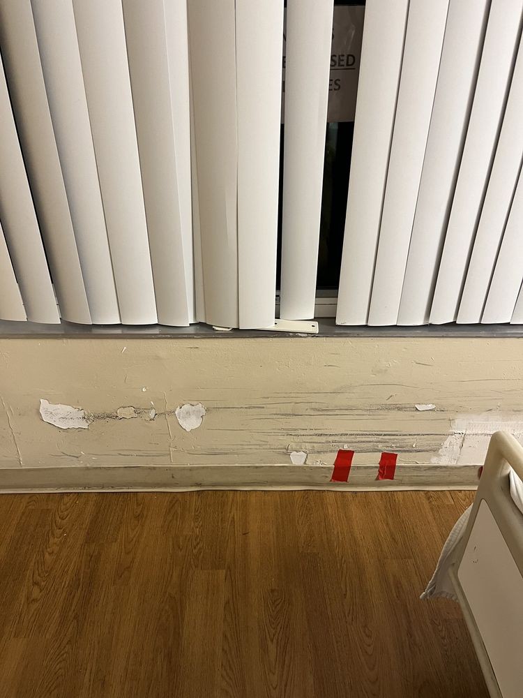A wall with visible damage and paint peeling beneath vertical blinds.