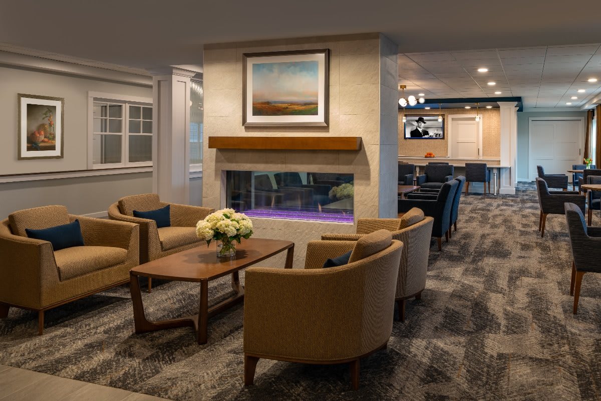 A cozy lounge area with modern seating around a central fireplace, accented by artwork and a carpeted floor.