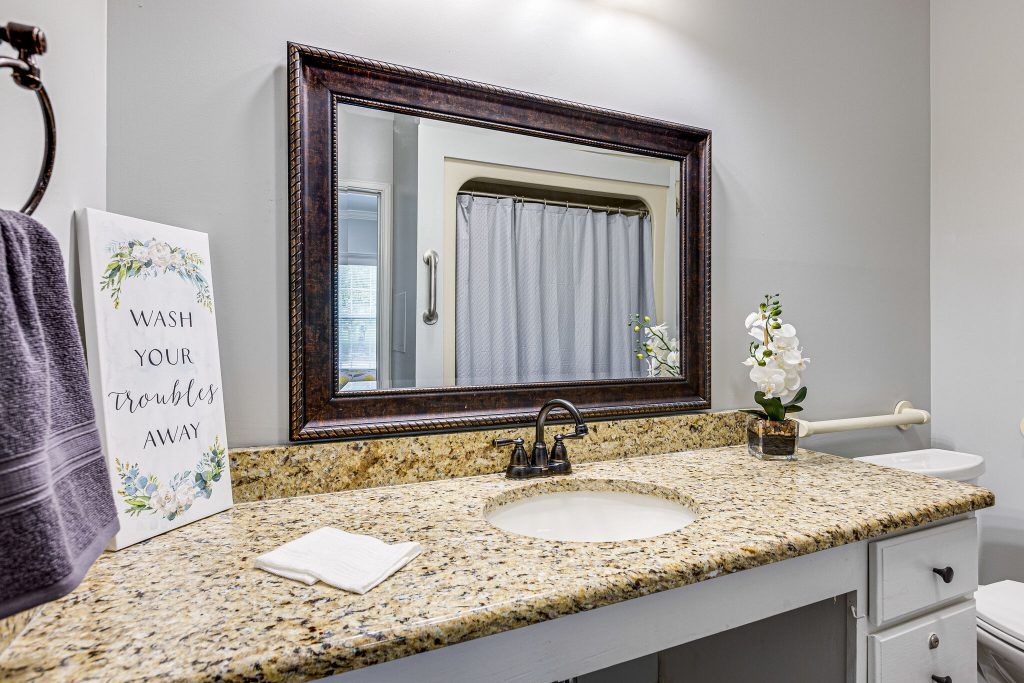 A bathroom with a granite countertop featuring a large framed mirror, sink, faucet, and decorative elements.