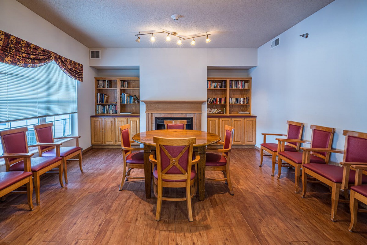 A cozy living room with a round wooden table surrounded by chairs, flanked by bookshelves and a fireplace.