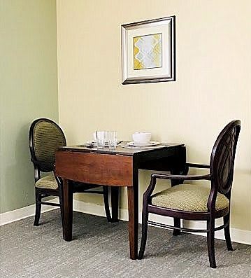 A small dining area with a wooden table and two upholstered chairs, adorned with a framed artwork on the wall.