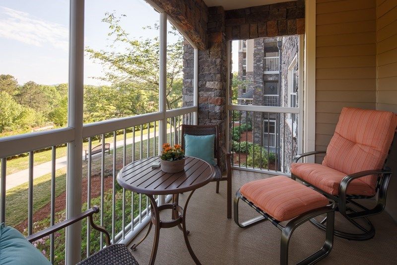 A cozy balcony with seating and a small table overlooking an apartment complex.