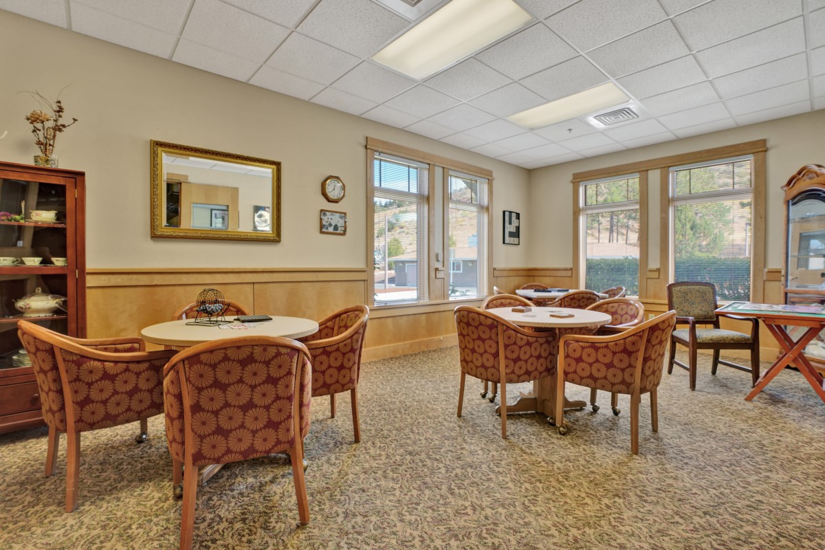 A cozy dining area with tables and patterned chairs surrounded by large windows and decorative elements.