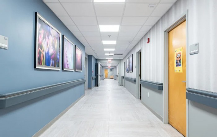 A brightly lit hospital corridor with artwork on the walls and doors leading to various rooms.