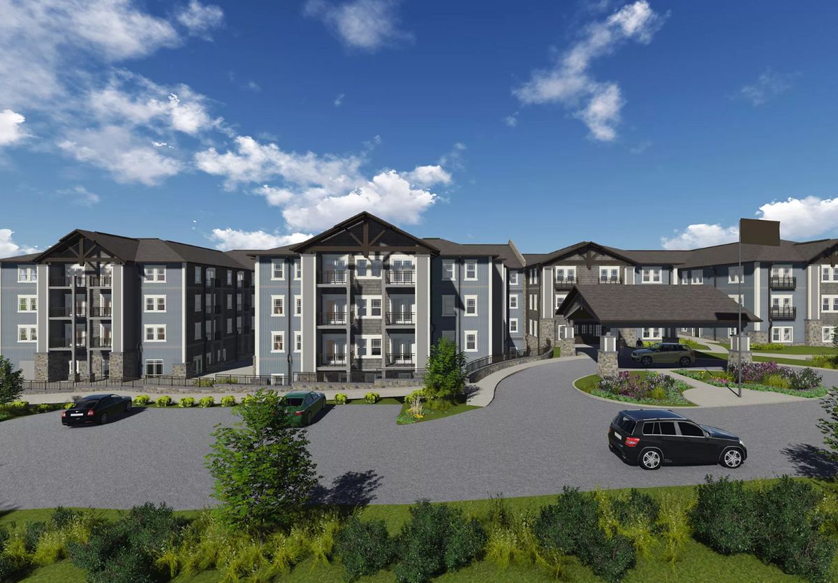 A modern apartment complex with landscaped surroundings and a spacious parking area under a clear blue sky.