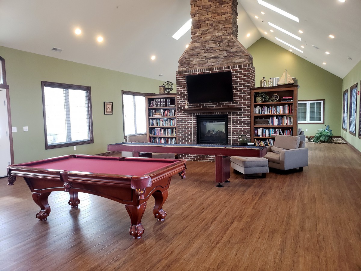 A spacious living room with a pool table, cozy fireplace, and built-in bookshelves.