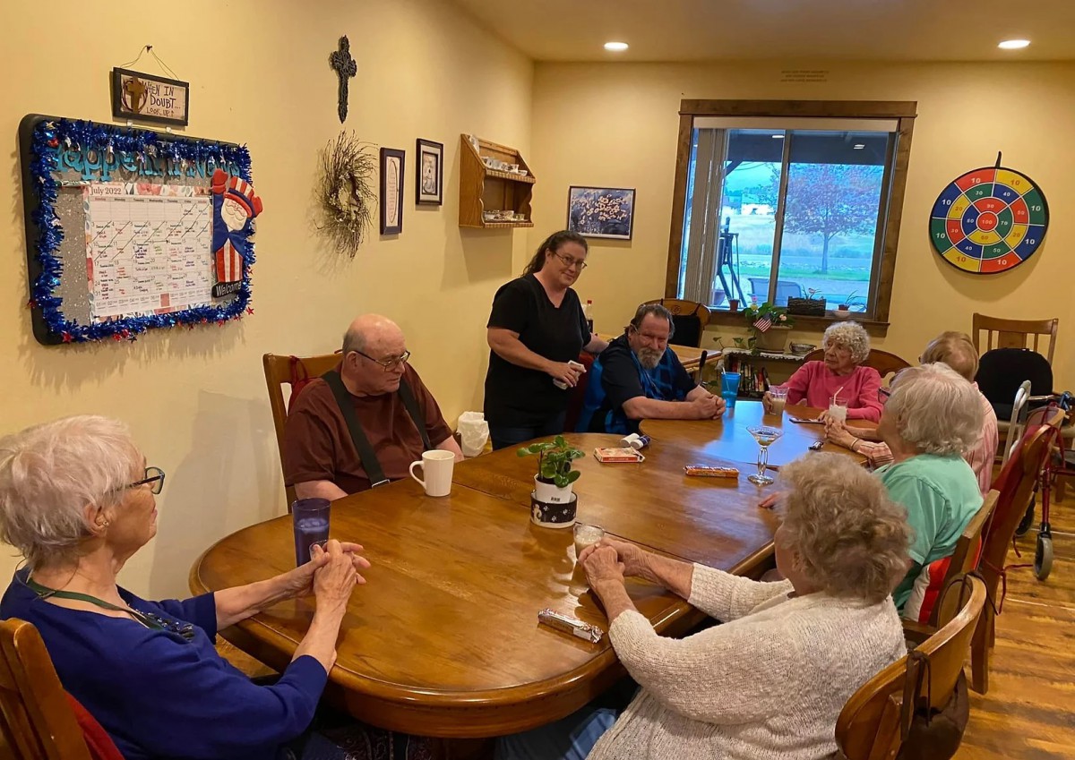 A group of seniors socializing around a table in a care home setting.