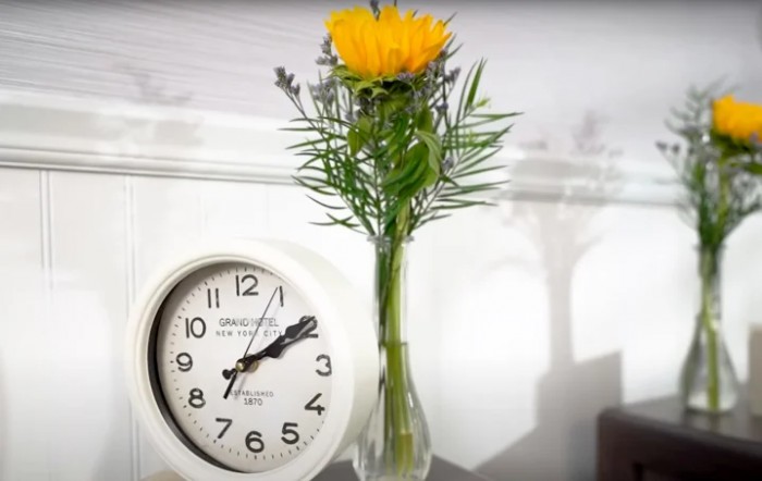 A yellow flower in a vase sits next to an analog clock, showcasing simple home decor.