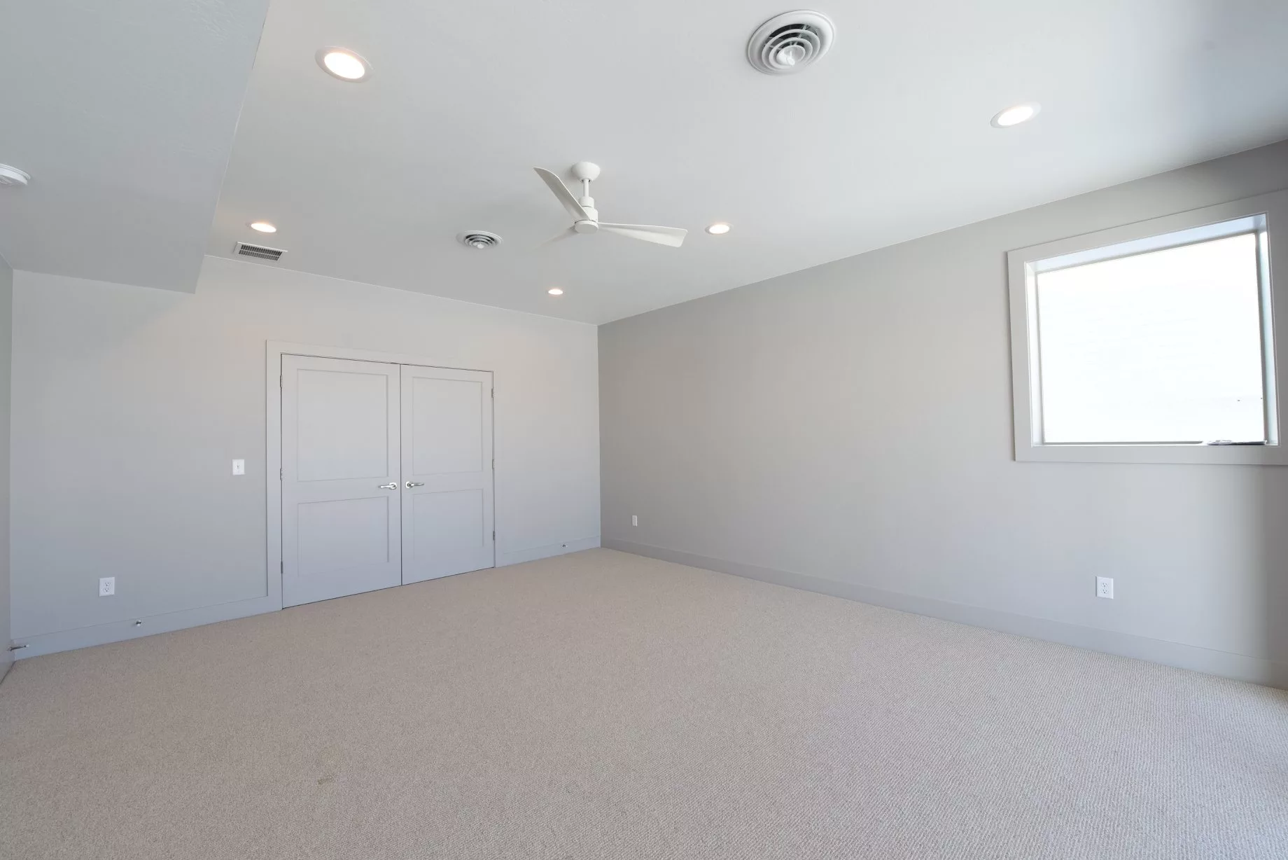 A minimalist empty room with neutral colors, featuring a carpeted floor and recessed lighting.