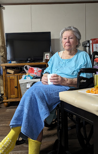 An elderly woman sitting in a wheelchair, enjoying a warm drink in her cozy living room.