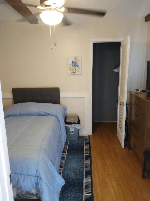 A small bedroom featuring a neatly made bed with blue bedding, a dresser, and an open closet.