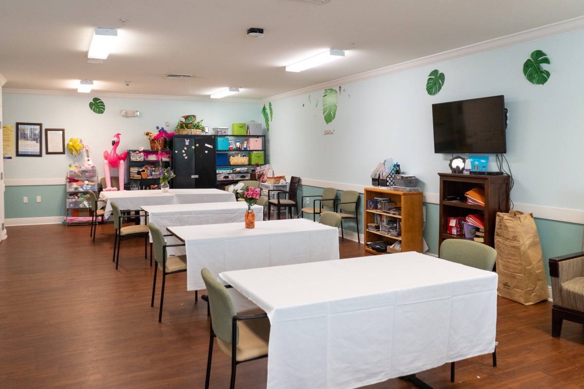 A bright classroom with neatly arranged tables covered in white tablecloths, decorated with colorful elements and a bookshelf.