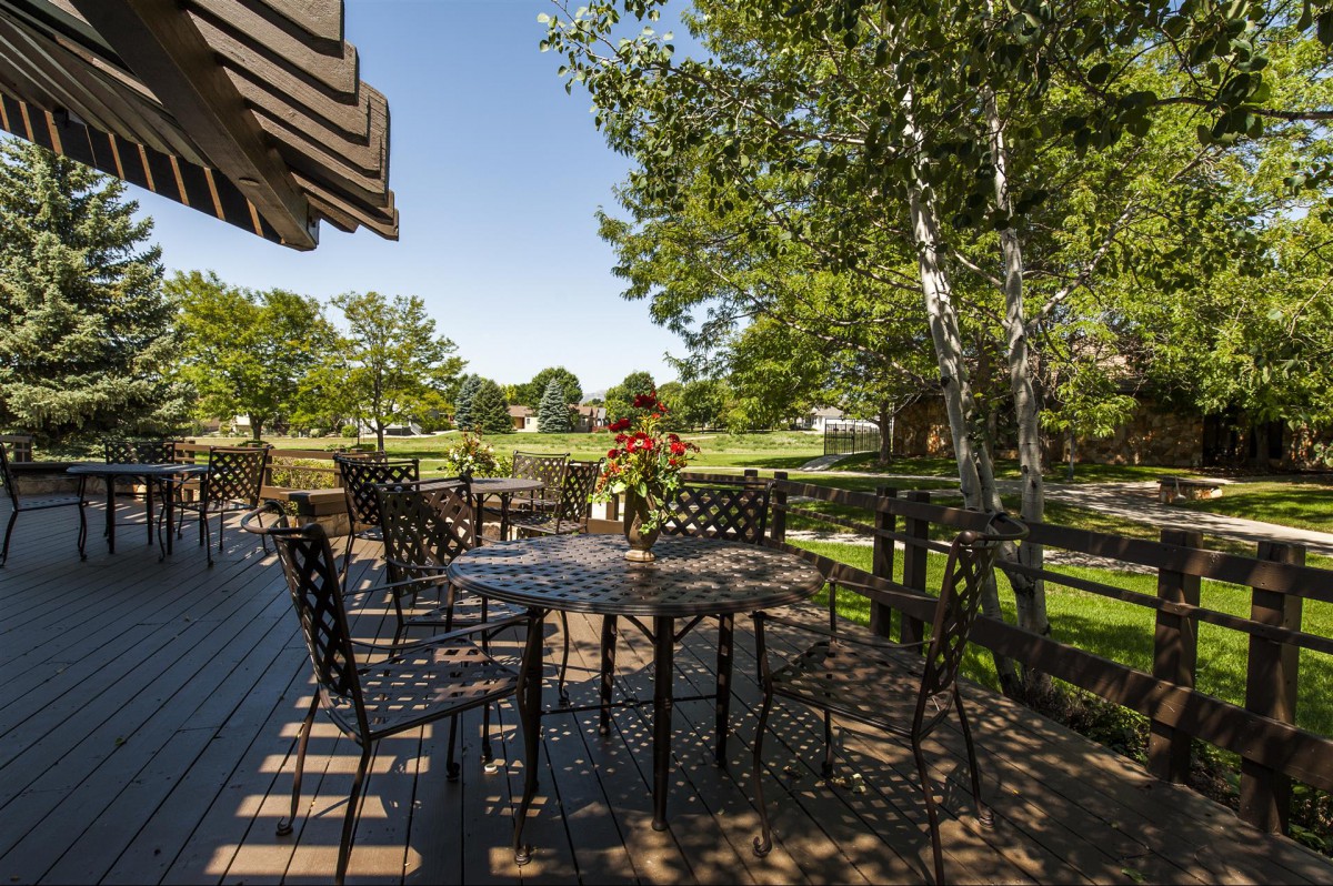 A sunny outdoor patio with tables and chairs, surrounded by lush greenery.