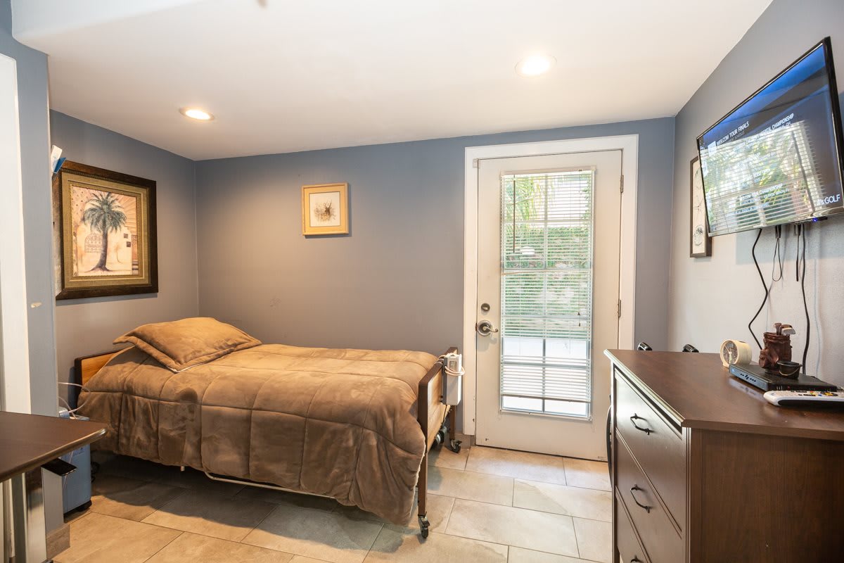 A cozy bedroom with a single bed, soft lighting, and a door leading outside.