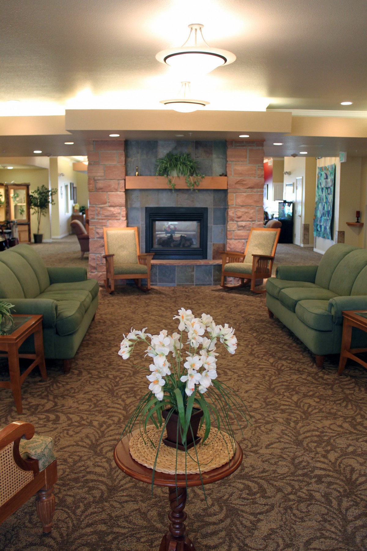 A cozy living room with sofas and a fireplace, adorned with an orchid centerpiece.