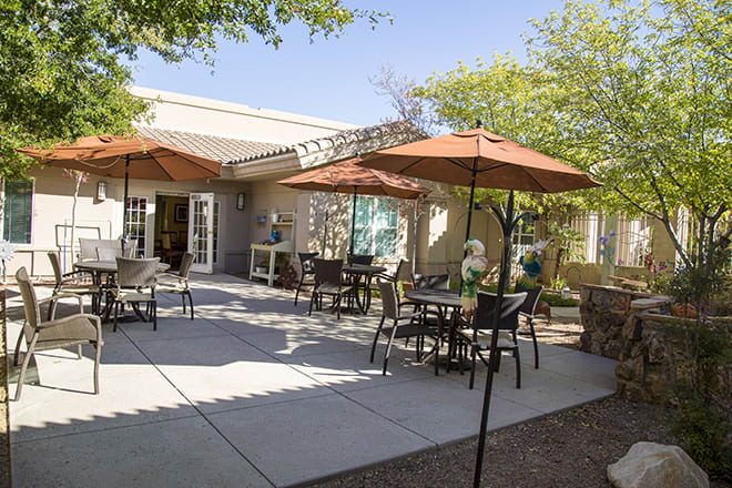 A sunny outdoor patio with tables, chairs, and umbrellas next to a building.